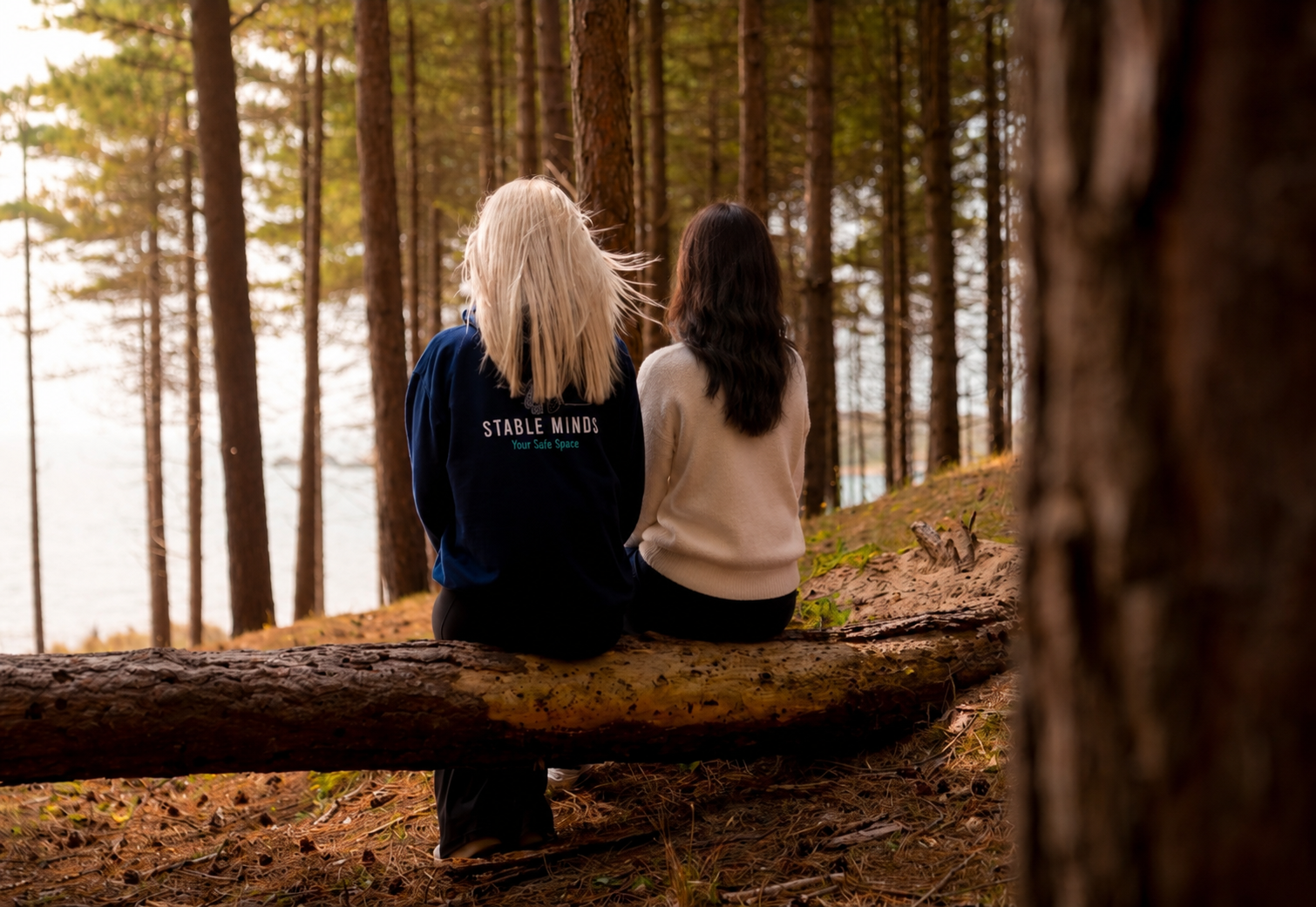 Milly and a client sitting together in woodland, seen from behind